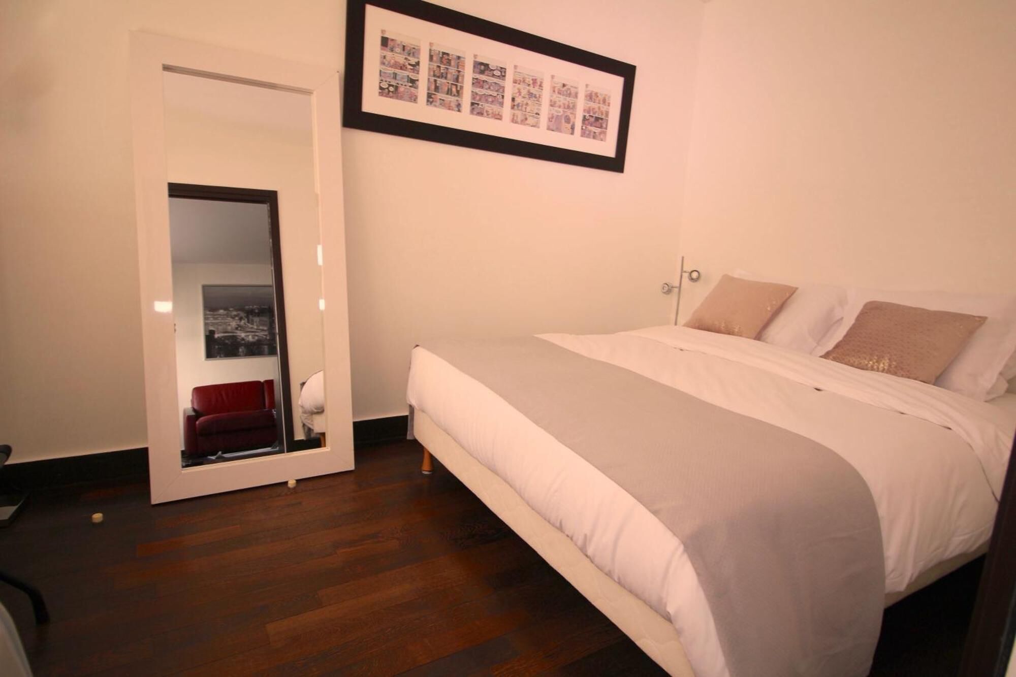 A bedroom with a bed, a red chair, a door, and a framed collage on the wall.
