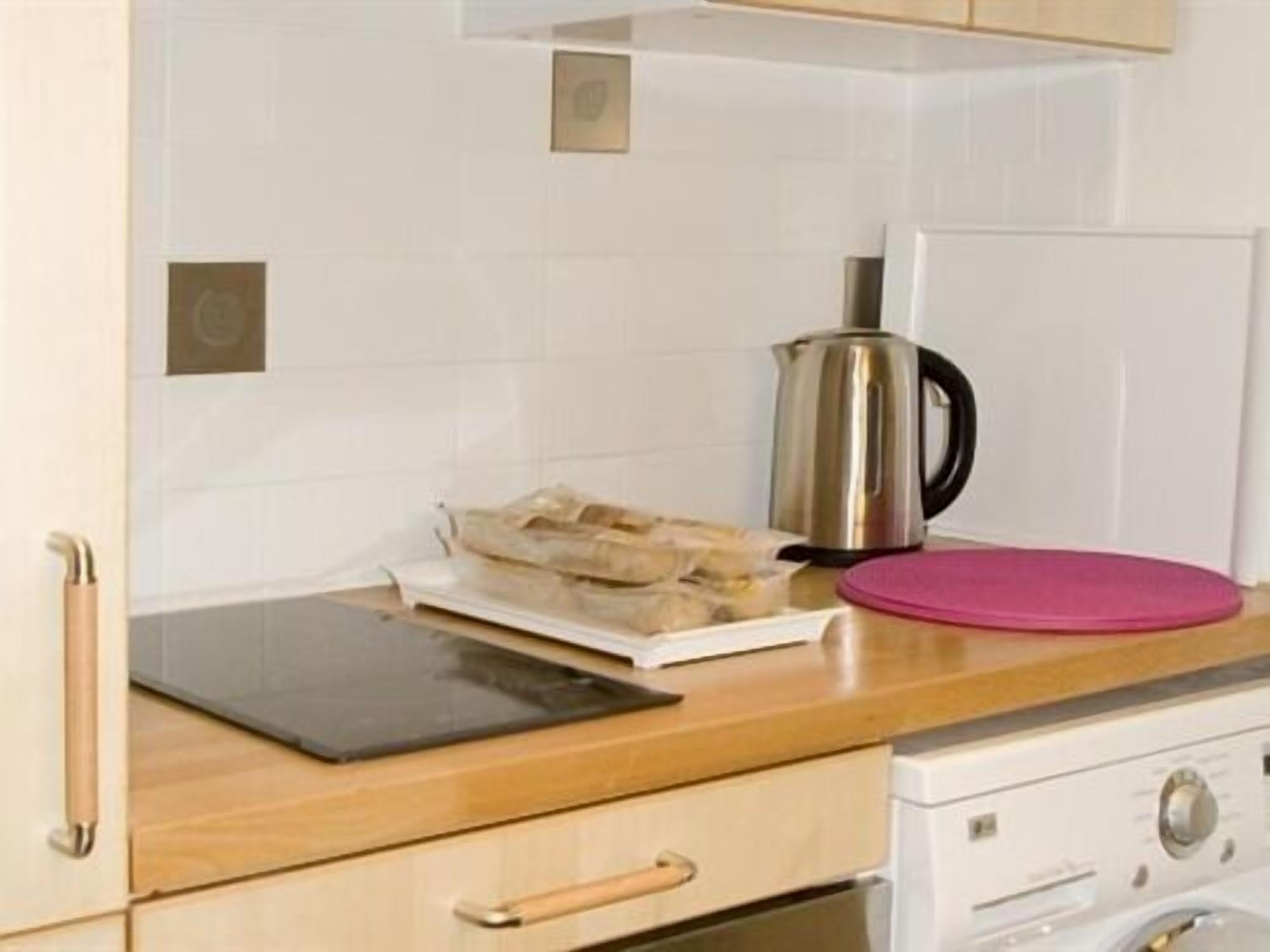 A kitchen with a stainless steel kettle, a pink cutting board, and a white refrigerator.
