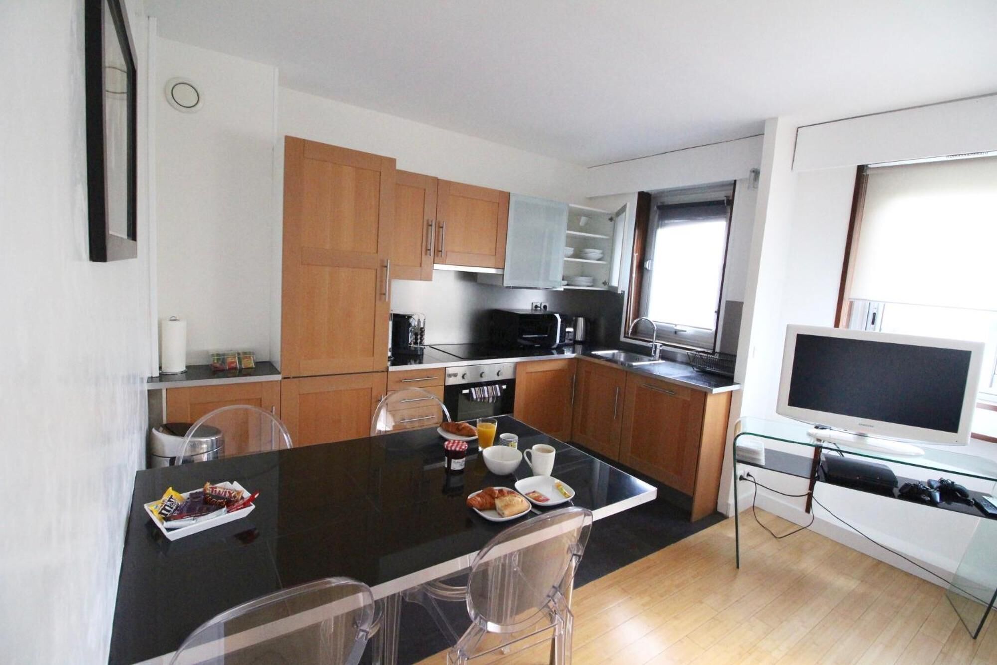 A compact kitchen with wooden cabinets, a black countertop, and a dining area with a glass table and chairs.