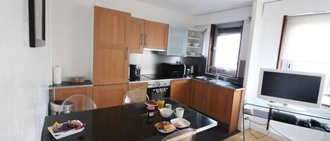 A compact kitchen with wooden cabinets, a black countertop, and a dining area with a glass table and chairs.