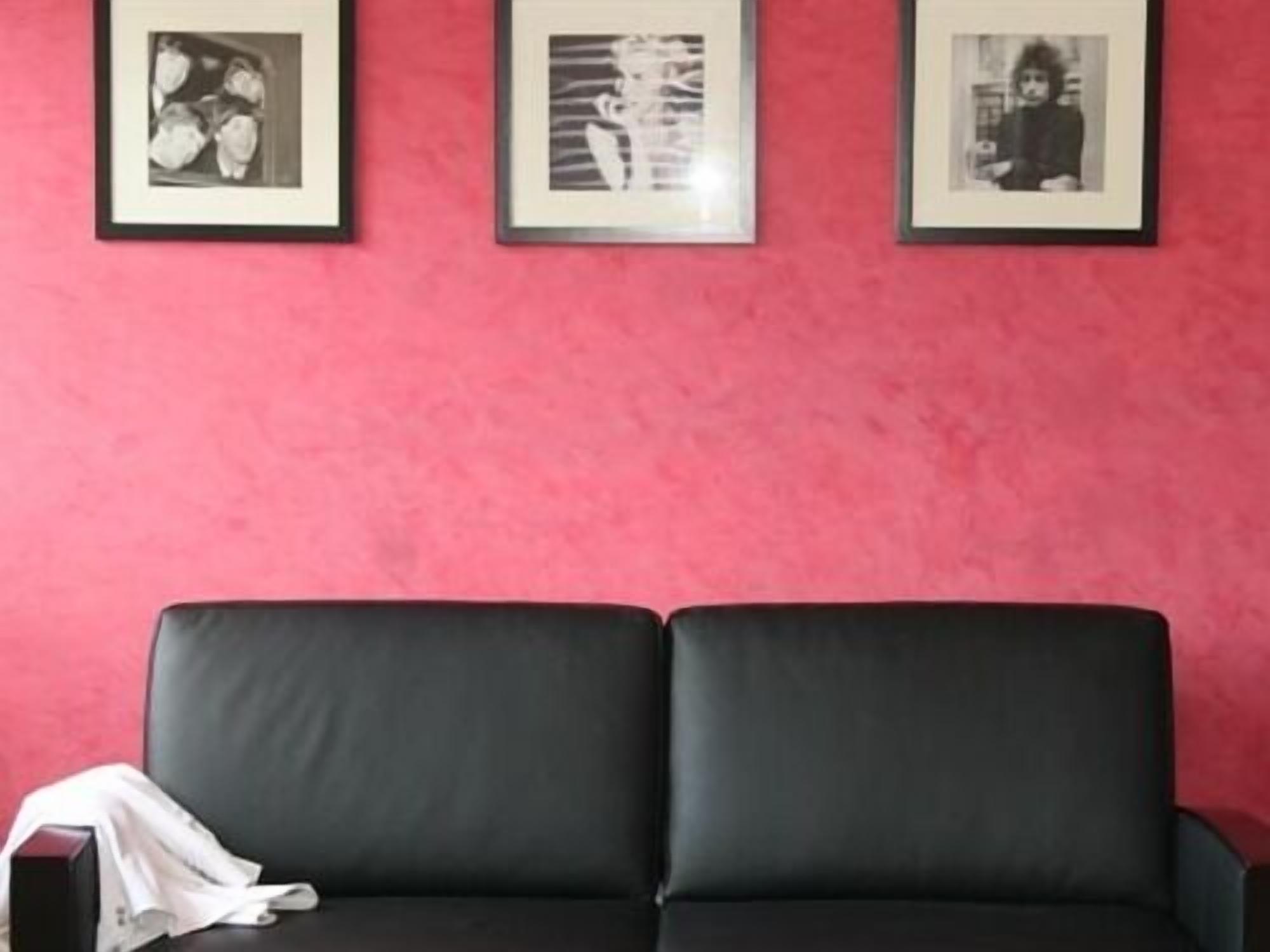 A room with a black sofa against a pink wall, three framed pictures, and a white cloth on the sofa.
