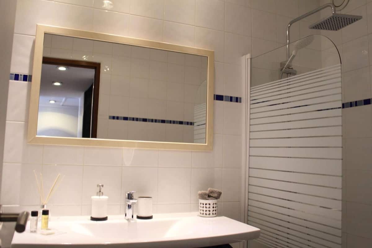 Un baño con un espejo grande, un lavabo, una ducha y un perchero para toallas.