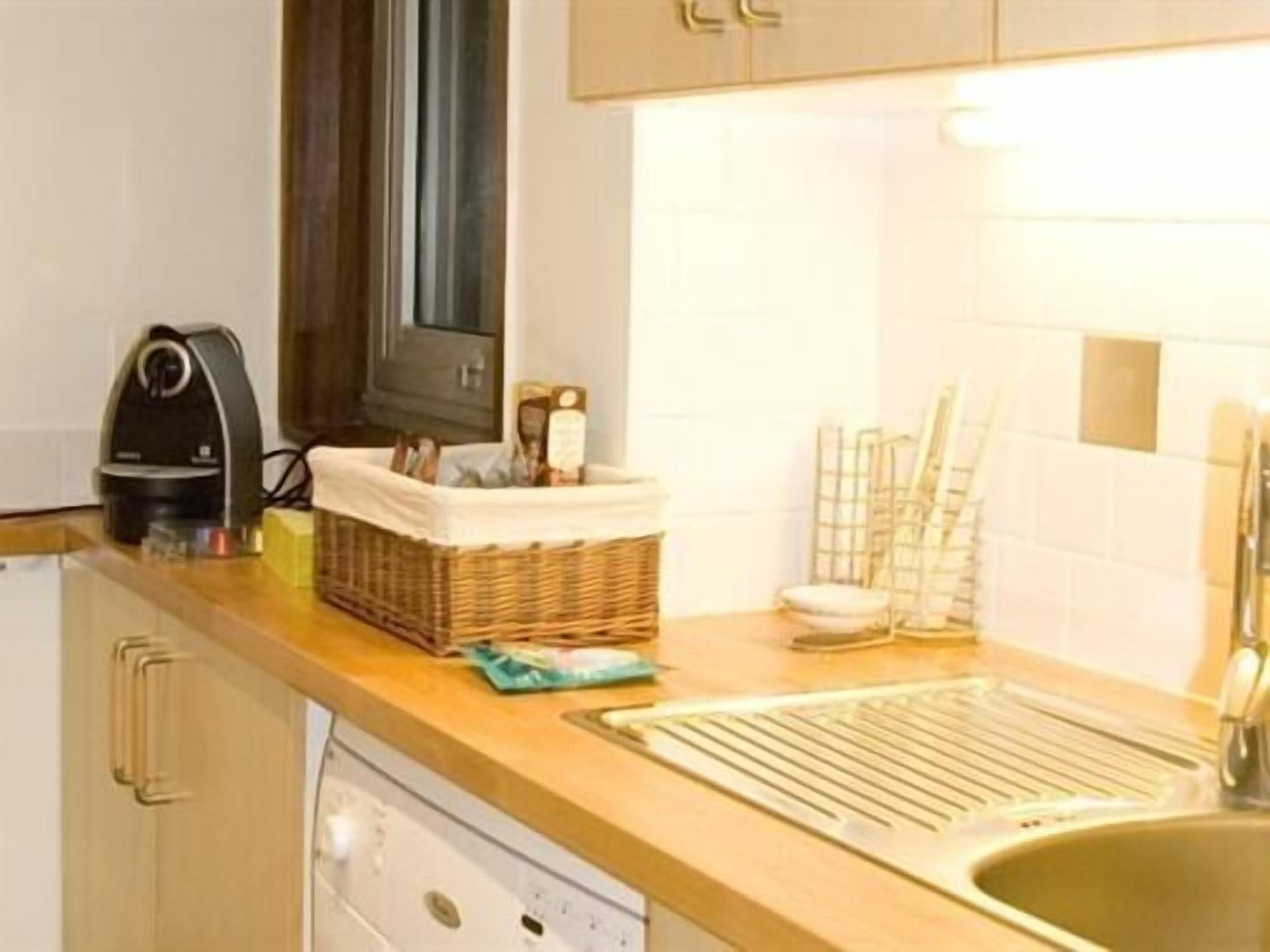 A kitchen with a wooden countertop, a coffee maker, a basket with kitchen utensils, and a sink.