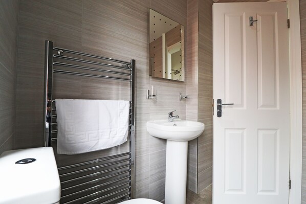A modern bathroom with a white toilet, a chrome towel rack with a white towel, a white pedestal sink, and a white door.