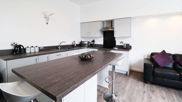A modern kitchen with a dark countertop, white cabinets, and a black stove. - Breck Blackpool (Blackpool)