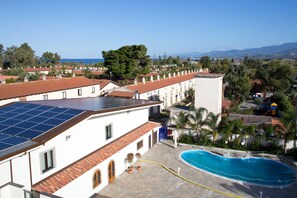 A residential area with a swimming pool, solar panels on a building, and a clear view of the sea. - Hotel Riviera Azzurra (Oliveri)