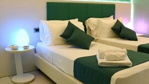 Ein Hotelzimmer mit zwei Betten, jeweils mit grüner Bettwäsche und Kissen, einem kleinen runden Tisch mit einer Lampe und einem ordentlich gefalteten Handtuch auf dem Bett.