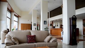 A spacious lobby with a beige sofa, a wooden coffee table, and a large clock. - Taybeh Golden Hotel (Taybeh)