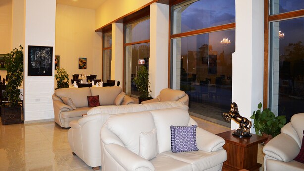 A spacious living room with large windows, a flat-screen TV mounted on the wall, and several sofas. - Taybeh Golden Hotel (Taybeh)