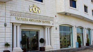 The exterior of the Taybeh Golden Hotel with a prominent crown logo, large glass entrance, and potted plants at the entrance. - Taybeh Golden Hotel (Taybeh)