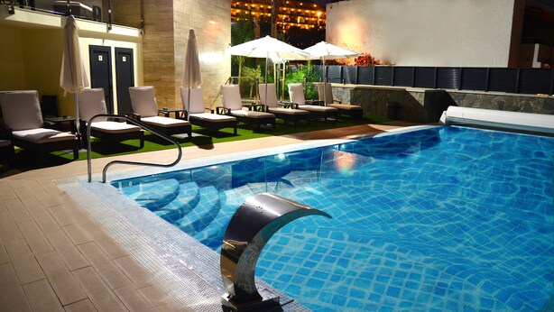 A swimming pool with lounge chairs and umbrellas, surrounded by a stone wall and a wooden deck. - Apartamentos Cataleya (San Bartolomé de Tirajana)