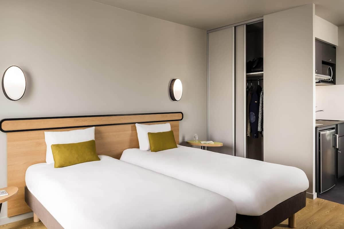 A hotel room with two beds, a wardrobe, a small table, and a built-in fridge.