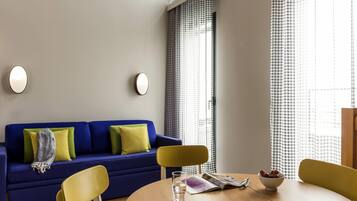 A modern living room with a blue sofa, yellow chairs, a wooden table, and a window with patterned curtains.