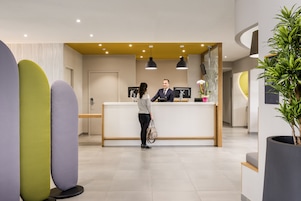 Un área de recepción de diseño moderno, con una mesa de recepción, una planta grande en maceta y un piso de baldosas limpias.
