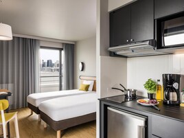 Una habitación de hotel pequeña con cama, kitchenette y vista a la ciudad desde la ventana.