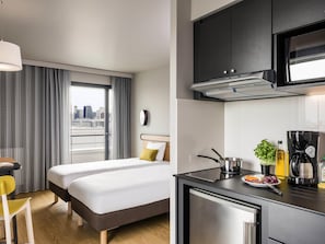 Una habitación de hotel pequeña con cama, kitchenette y vista a la ciudad desde la ventana.