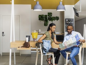 A modern kitchen with a dining table, chairs, a fruit drink dispenser, and a laptop. - Aparthotel Adagio Access Colombes La Défense (Colombes)