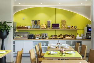 Un restaurante moderno con una pared amarilla curvada, mesas y sillas de madera. Hay varios alimentos y condimentos en la barra.