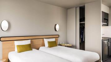 Une chambre d’hôtel avec deux lits, une armoire, une petite table et un réfrigérateur encastré.