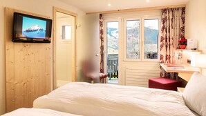 Une chambre d’hôtel comprenant un lit, un téléviseur fixé au mur, un bureau avec une chaise et une fenêtre avec des rideaux.