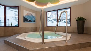 Un espace bien-être avec un bain à remous, de grandes fenêtres offrant une vue sur le paysage enneigé et un tableau représentant des montagnes.