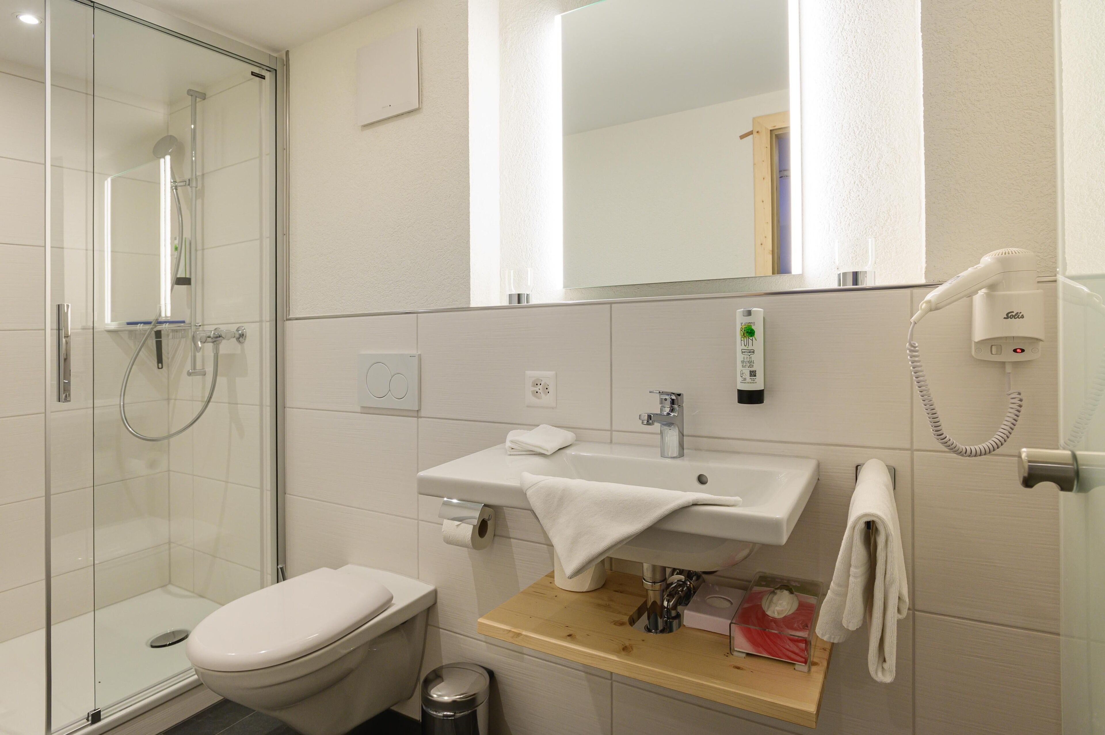 A modern bathroom with a glass shower enclosure, a toilet, a sink with a towel, and a hairdryer on the wall.