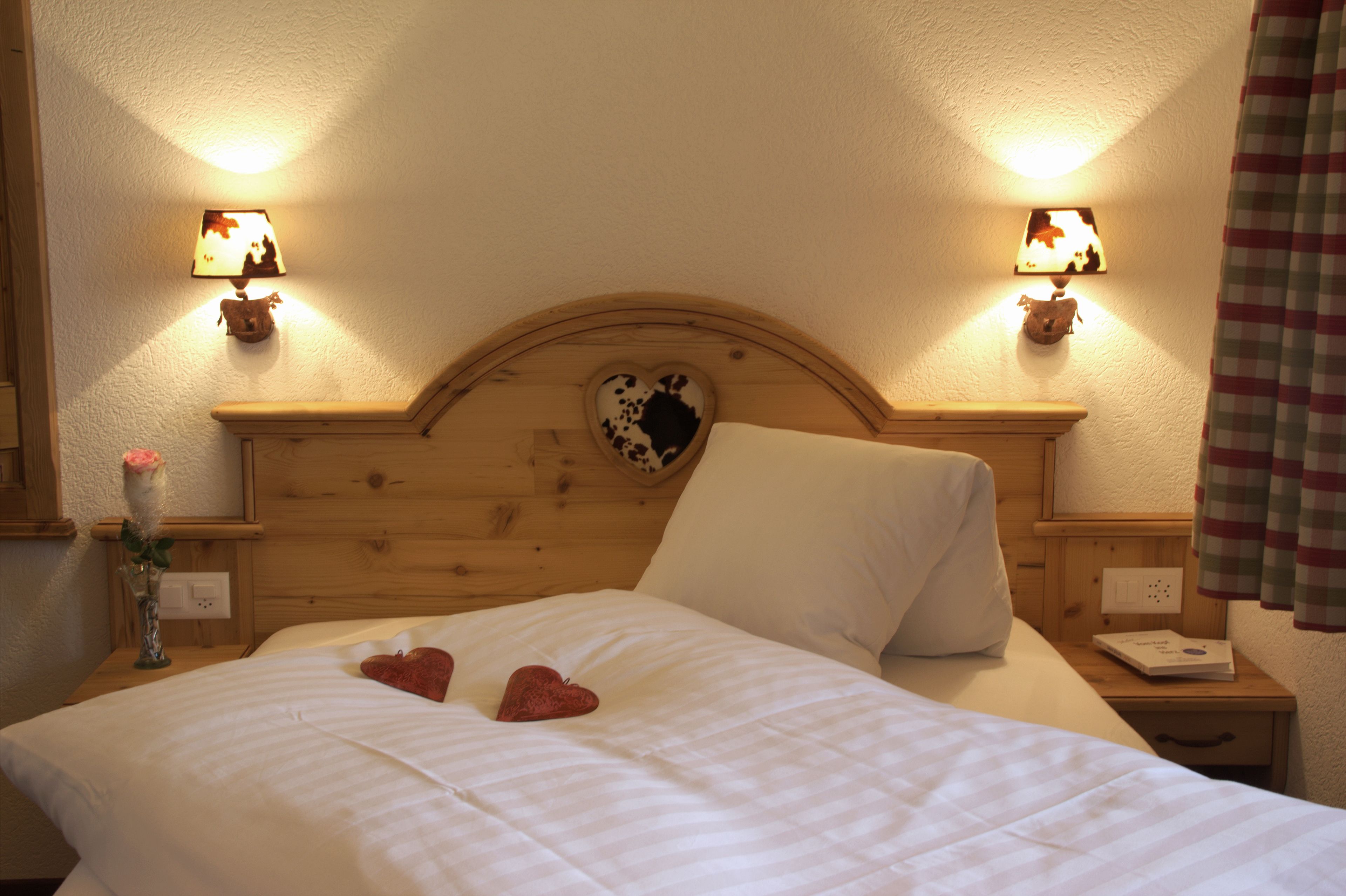 A neatly made bed with heart-shaped pillows, a wooden headboard with a heart-shaped mirror, and two bedside lamps.