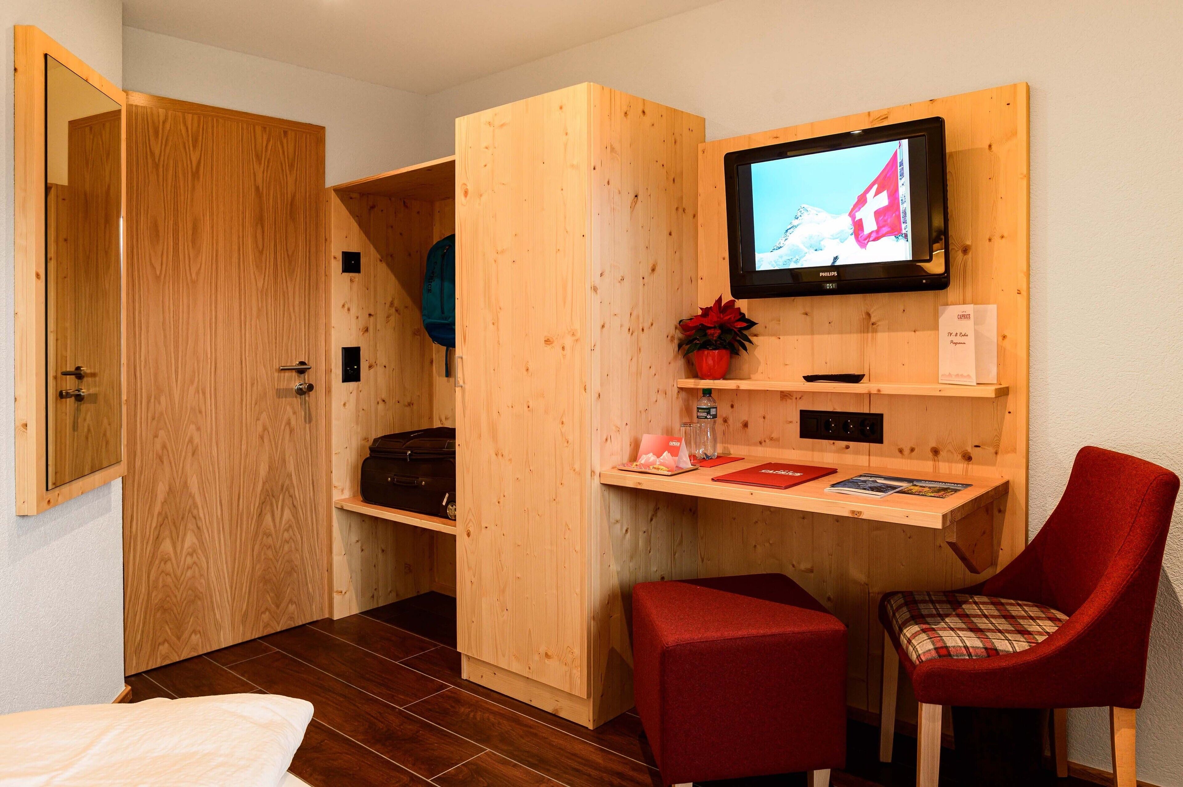 Ein Zimmer mit Holzboden, einem Fernseher, einem kleinen Tisch, einem roten Sessel und einem Bett.