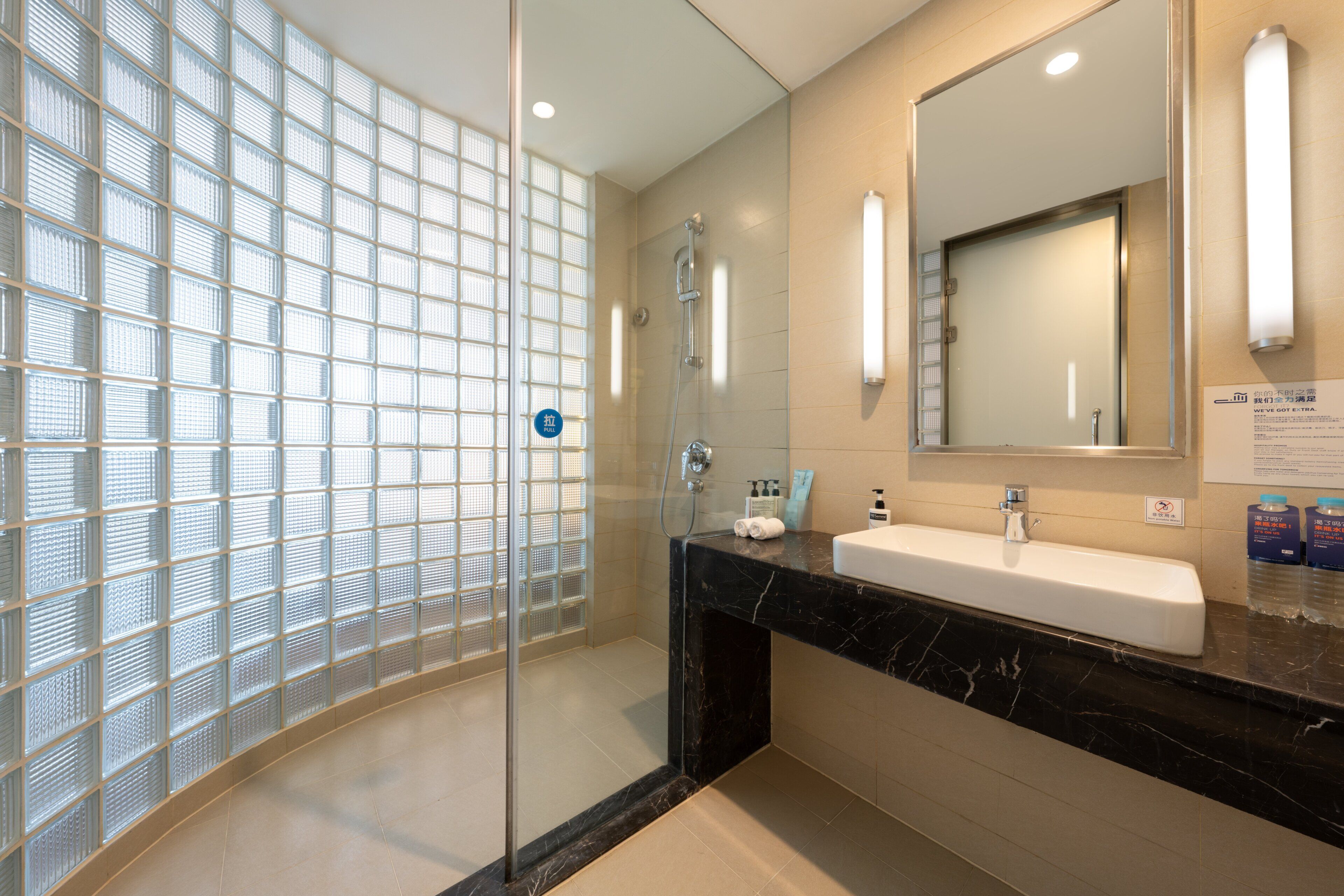 Une salle de bain moderne avec une douche à parois de verre, un comptoir en marbre, un grand miroir et un luminaire fixé au mur.