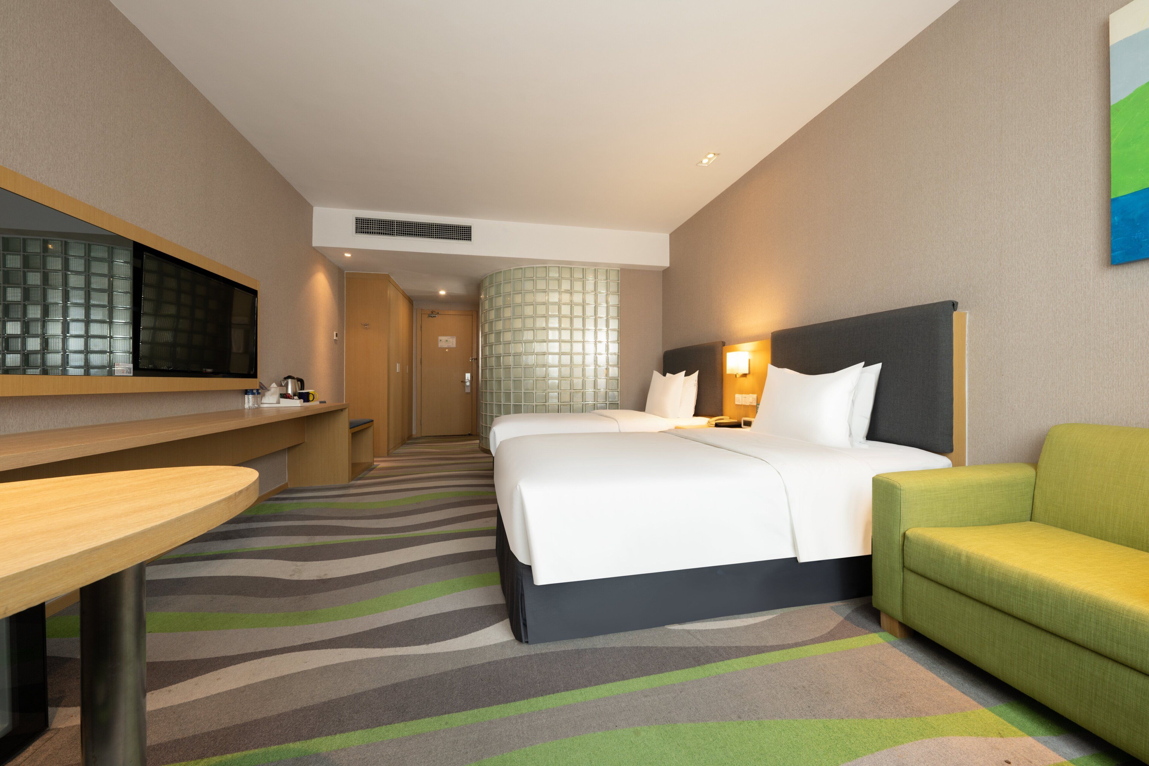 Una habitación de hotel con una cama, un sofá verde, un escritorio y un espejo grande.