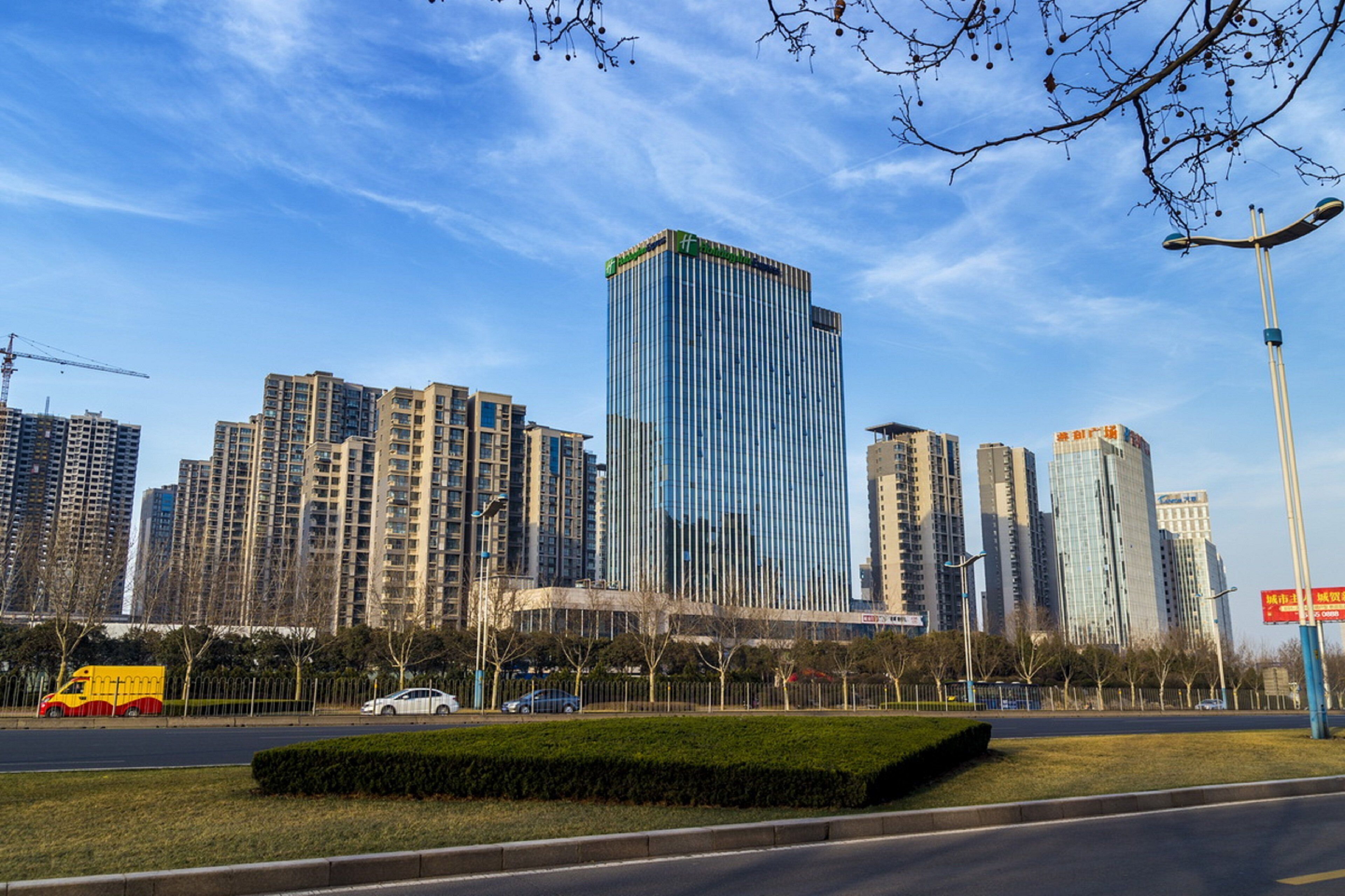 A cityscape with modern high-rise buildings, a clear sky, and a well-maintained urban park area.