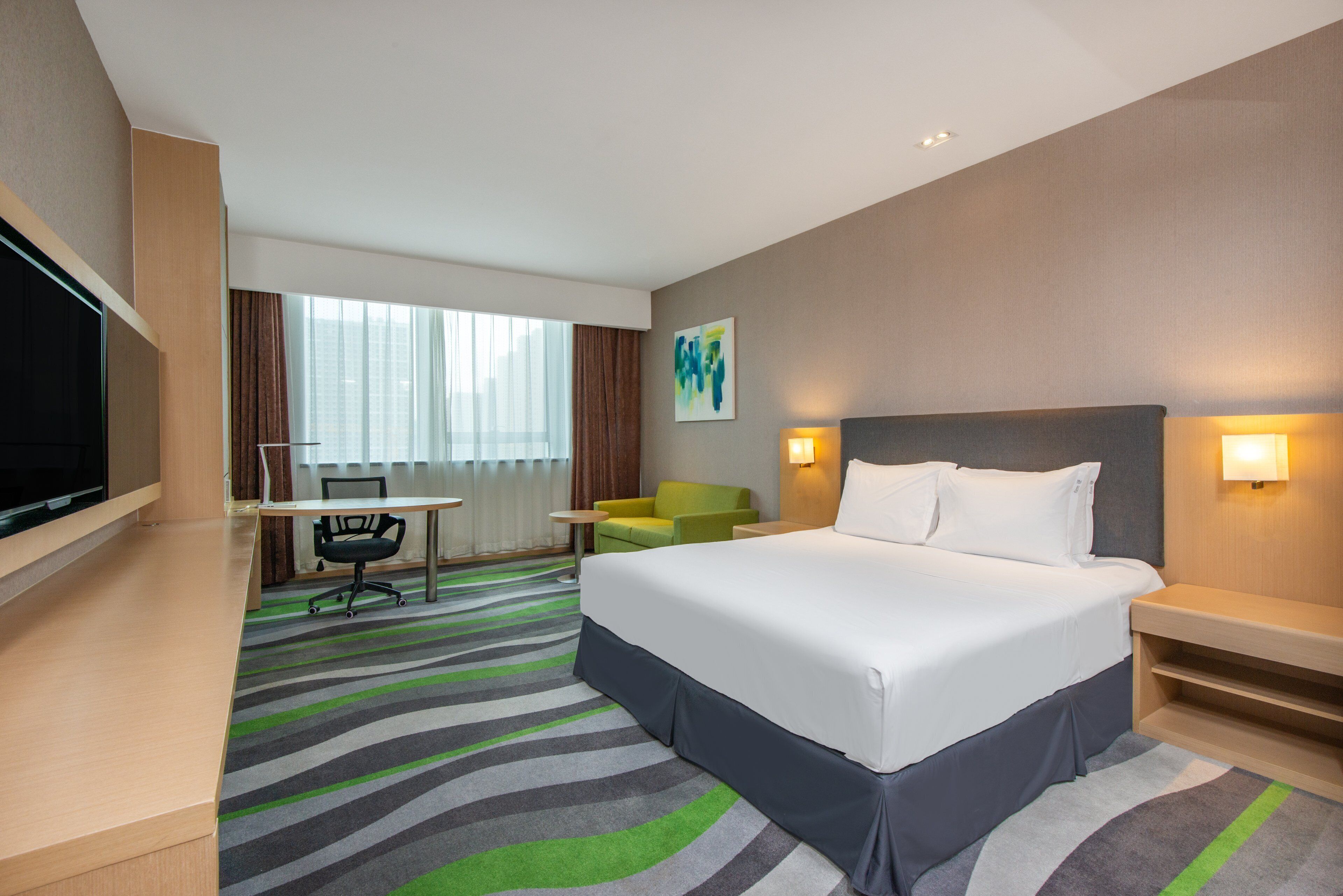 Ein Hotelzimmer mit Bett, Schreibtisch, Sessel, Fernseher und einem Fenster mit Vorhängen.