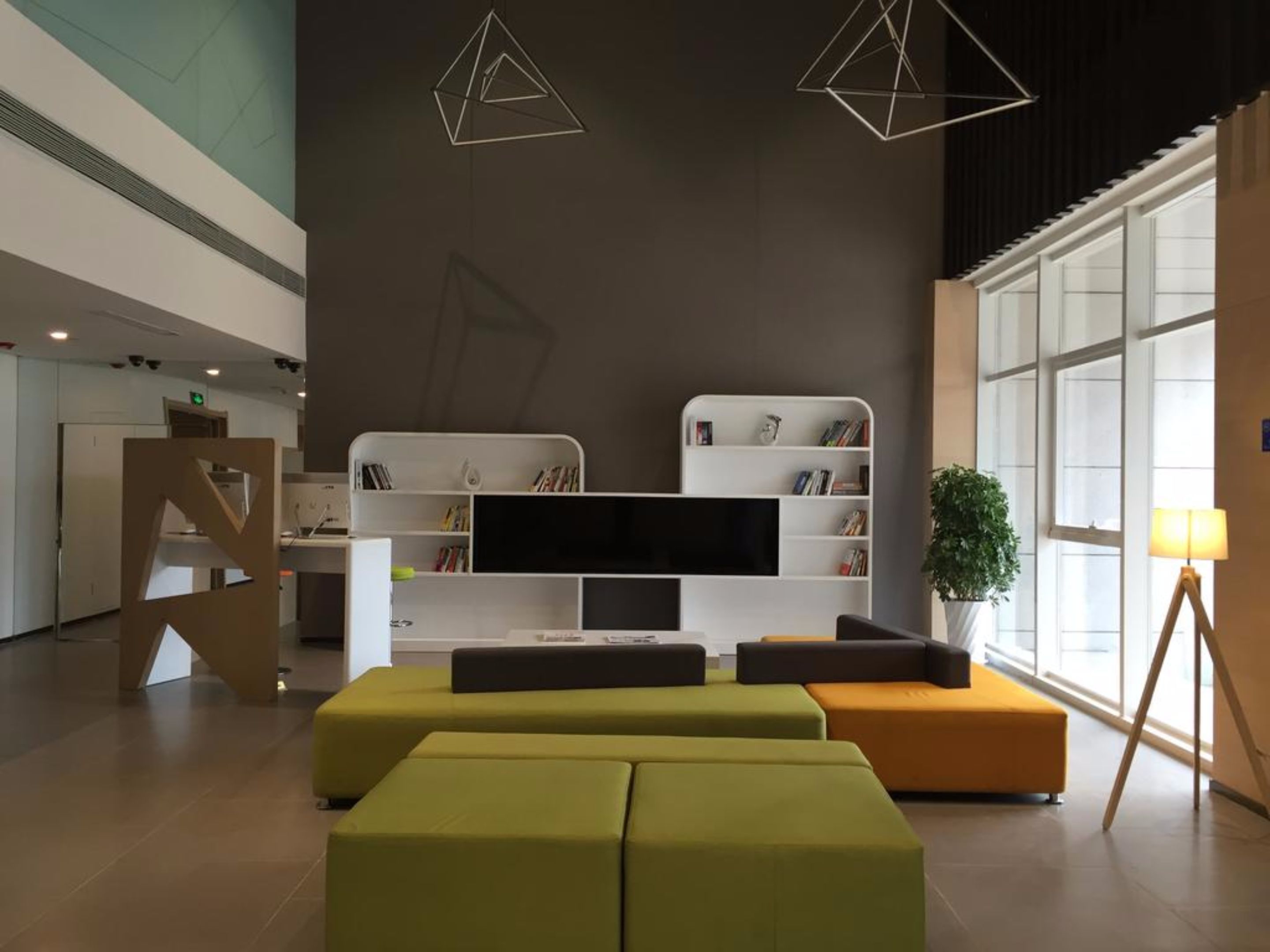 A modern living room with a large flat-screen TV, a white entertainment unit, and green and orange seating.