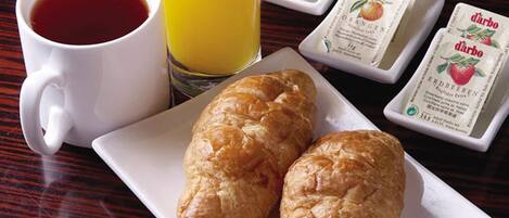 Ein Frühstückstisch mit einer Tasse Kaffee, einem Glas Orangensaft, zwei Croissants und Milch- und Marmeladepäckchen.