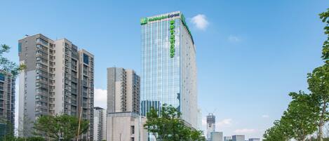 Een modern hoog hotel met een glazen gevel, omringd door andere gebouwen en een heldere lucht.