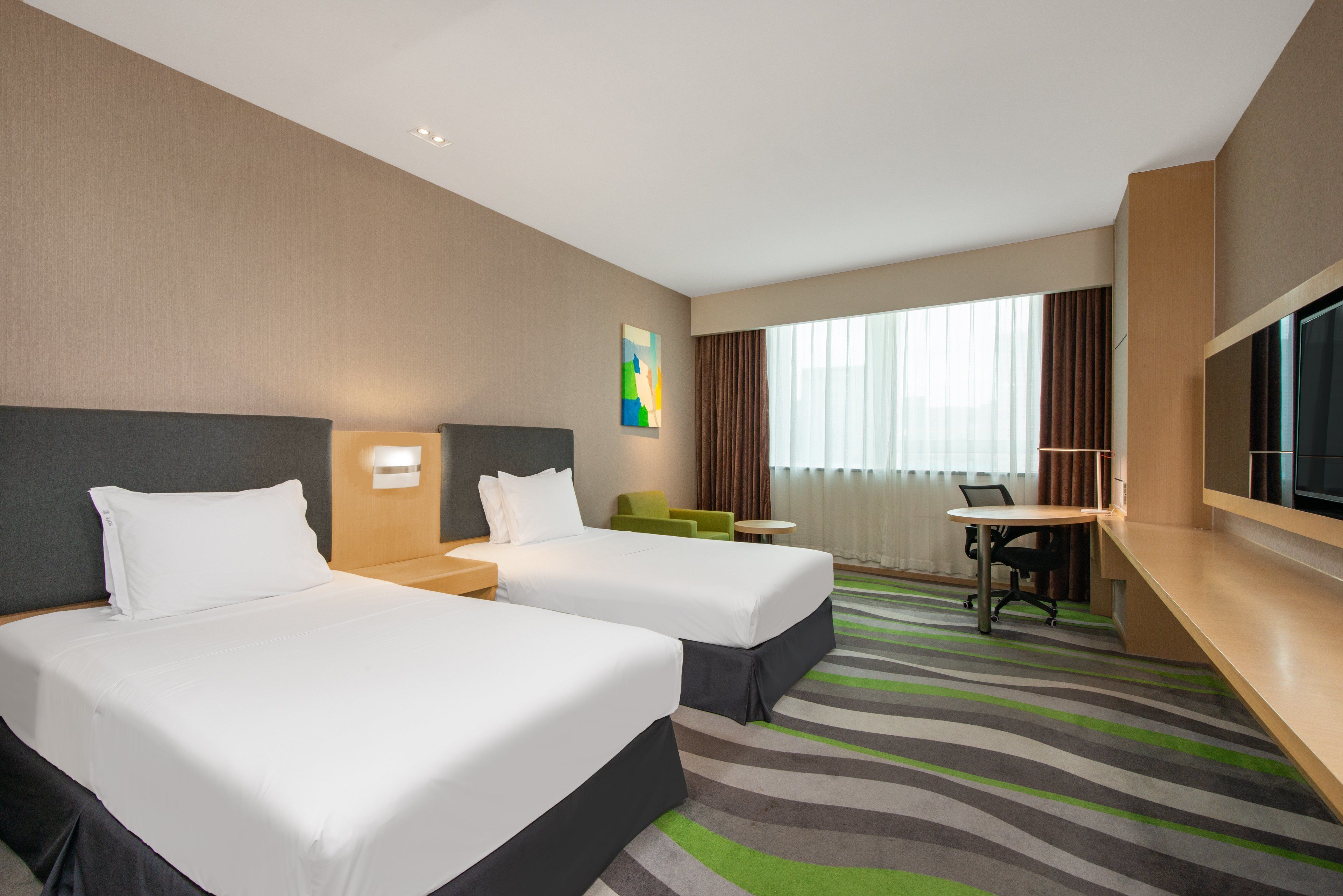 Une chambre d’hôtel avec deux lits, un bureau, une chaise, une télévision et une grande fenêtre avec des rideaux.