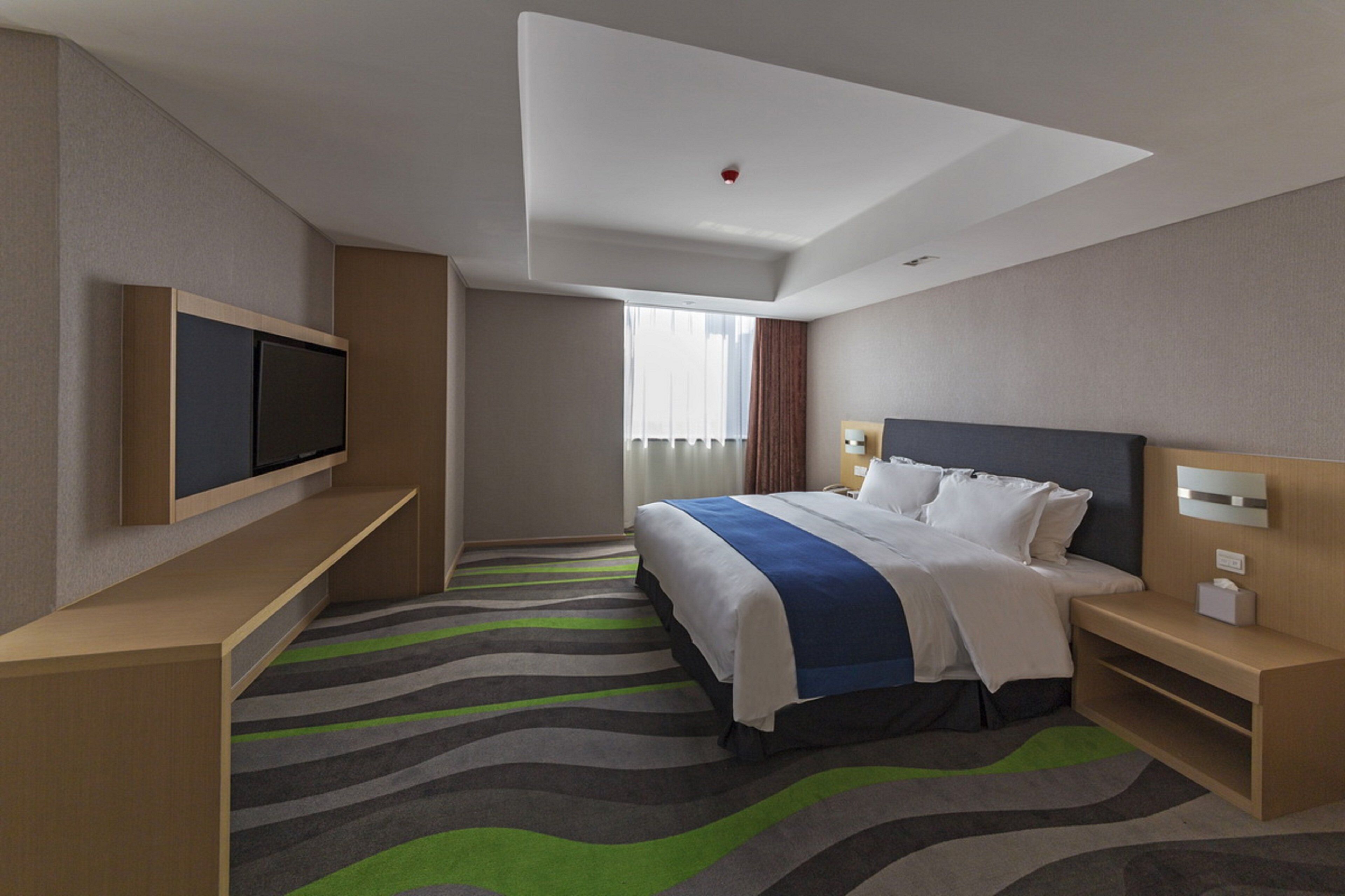 A hotel room with a bed, a TV, a desk, and a window with curtains.