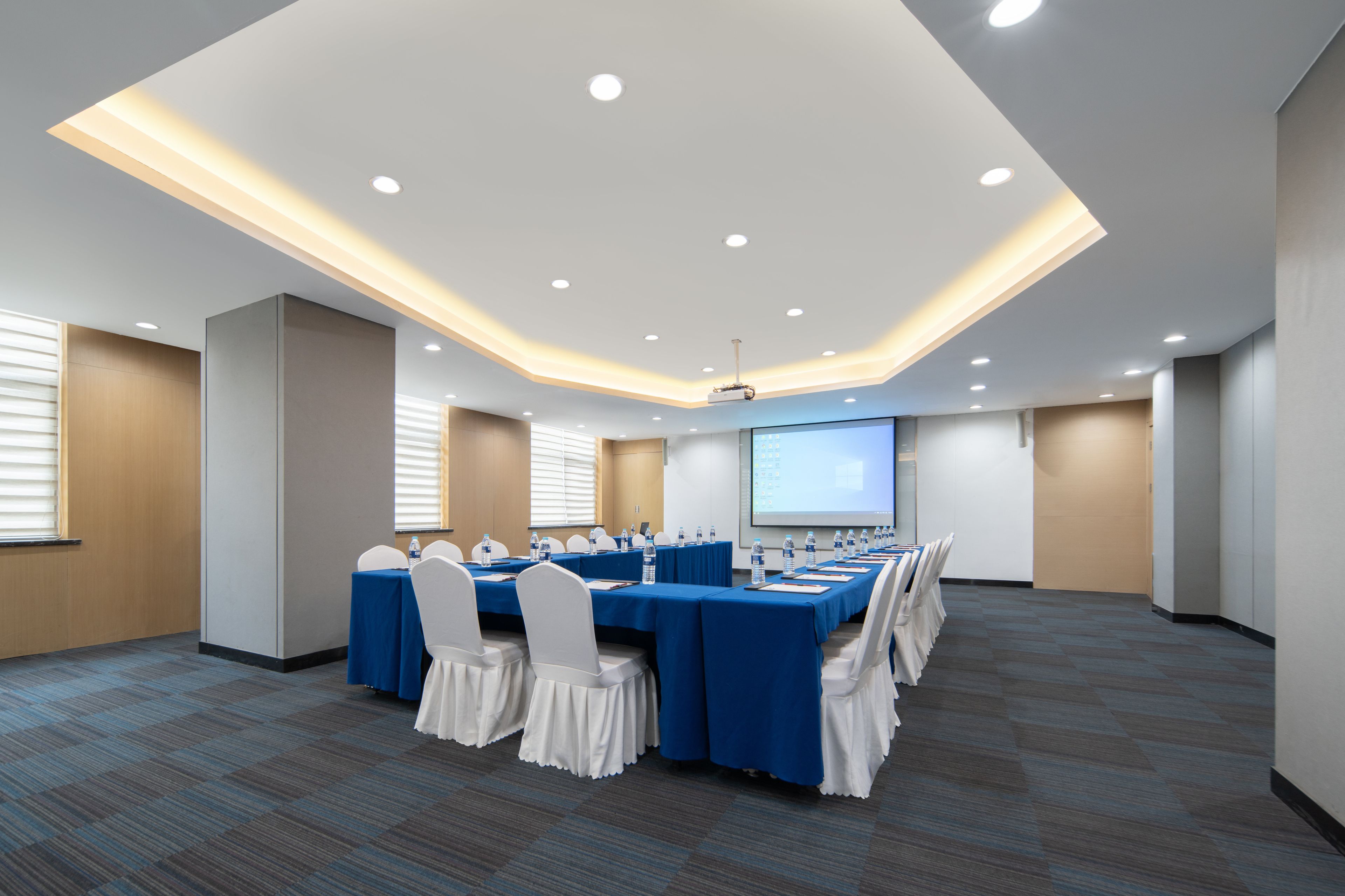 A conference room with a long table, chairs, and a projector screen.