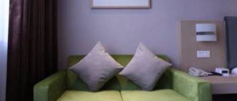 Una habitación de hotel moderna con un sofá verde, una mesa de centro redonda y un cuadro enmarcado en la pared.