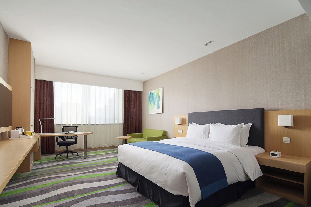Une chambre d’hôtel équipée d’un lit, d’un bureau, d’une chaise et offrant une vue sur l’extérieur.