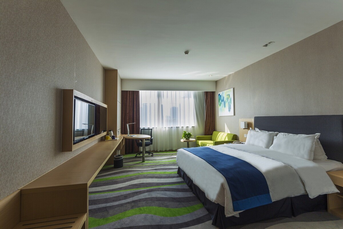 Une chambre d’hôtel équipée d’un lit, d’un bureau, d’une chaise, d’une télévision et d’une fenêtre avec des rideaux.