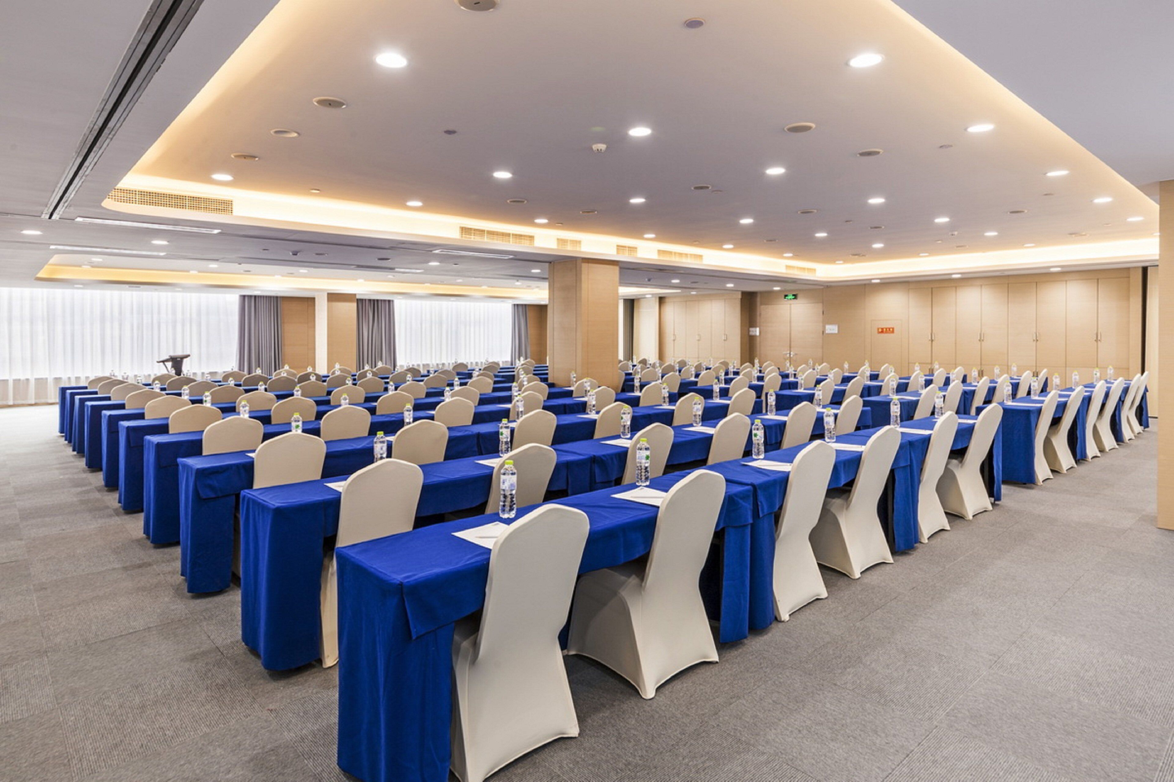Une salle de conférence avec des rangées de tables, de chaises et un éclairage au plafond.
