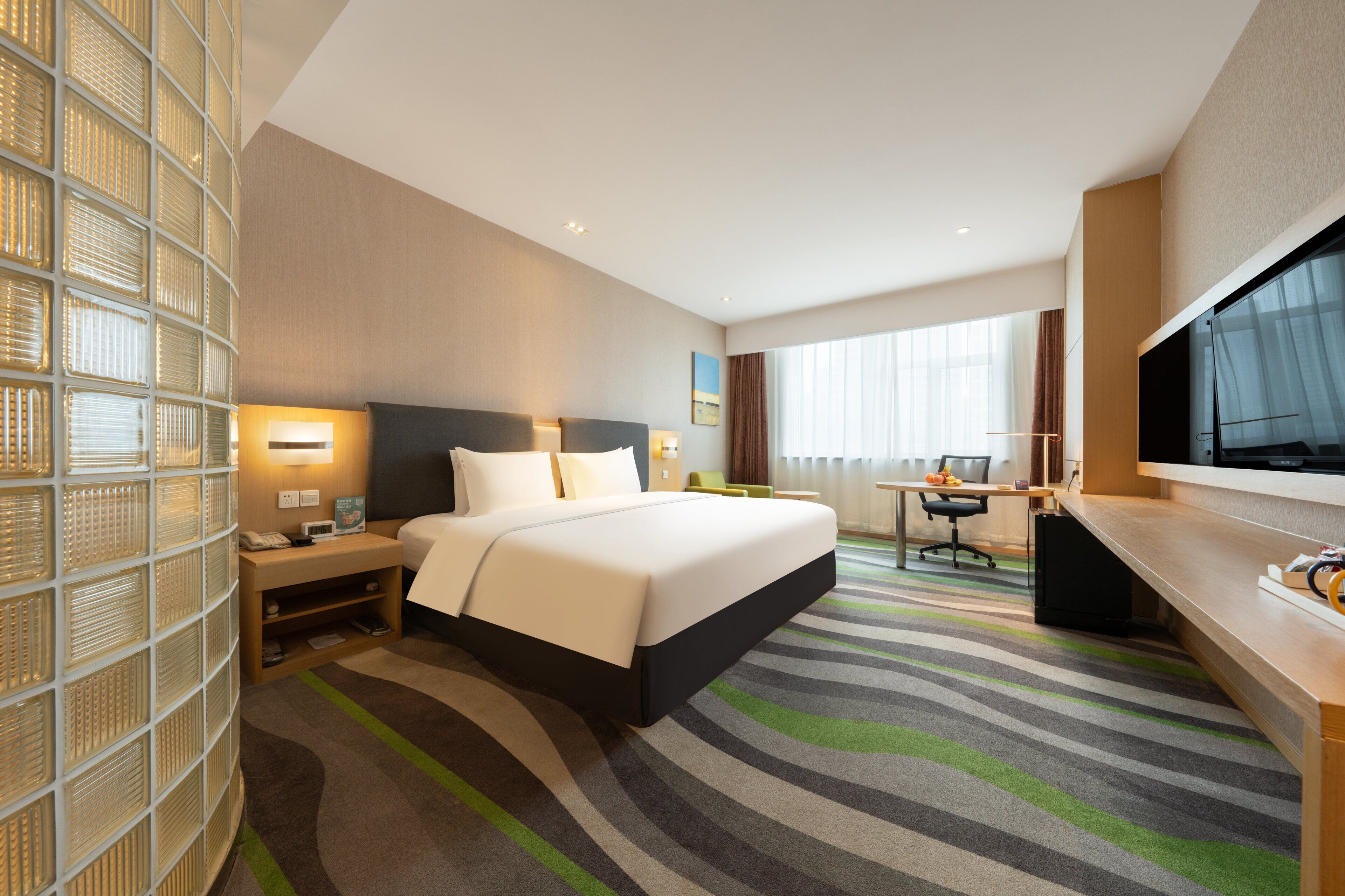 A hotel room with a bed, desk, TV, and a large window.