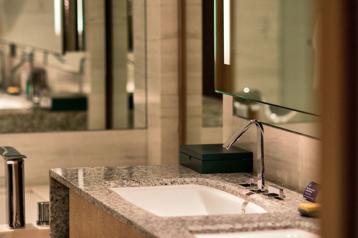 Un baño moderno con encimera de granito, un lavabo blanco y un espejo grande.