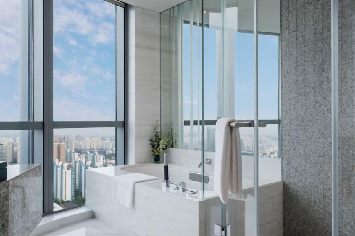 A modern bathroom with a large window, a bathtub, and a mirror.