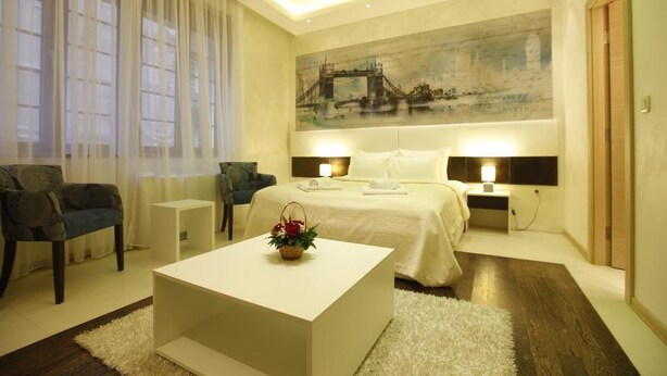 A modern hotel room with a large bed, two bedside tables with lamps, a white coffee table, and a large painting of a bridge on the wall. - City Code Exclusive (Belgrade)