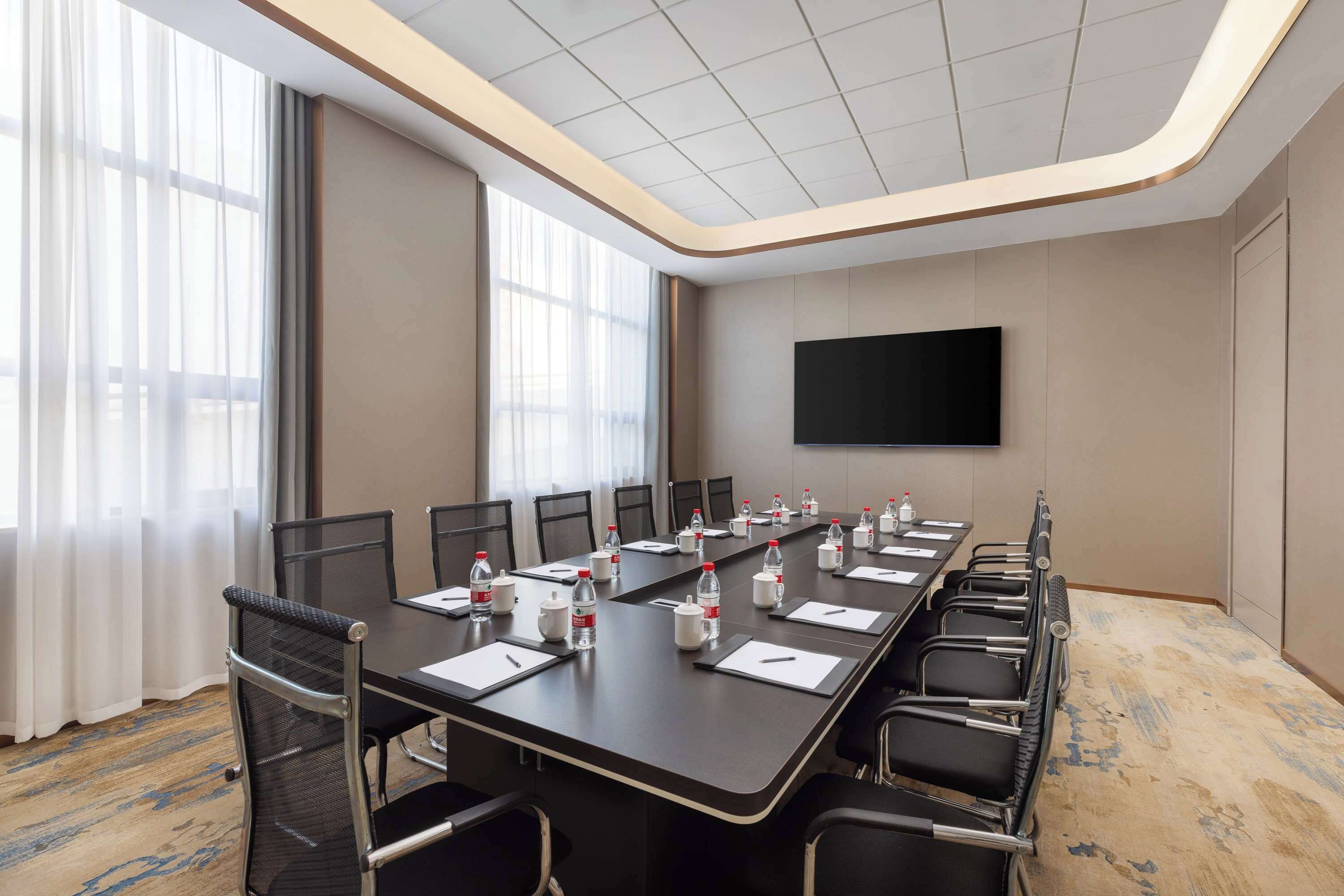 A conference room with a long table, chairs, water bottles, and a TV on the wall.