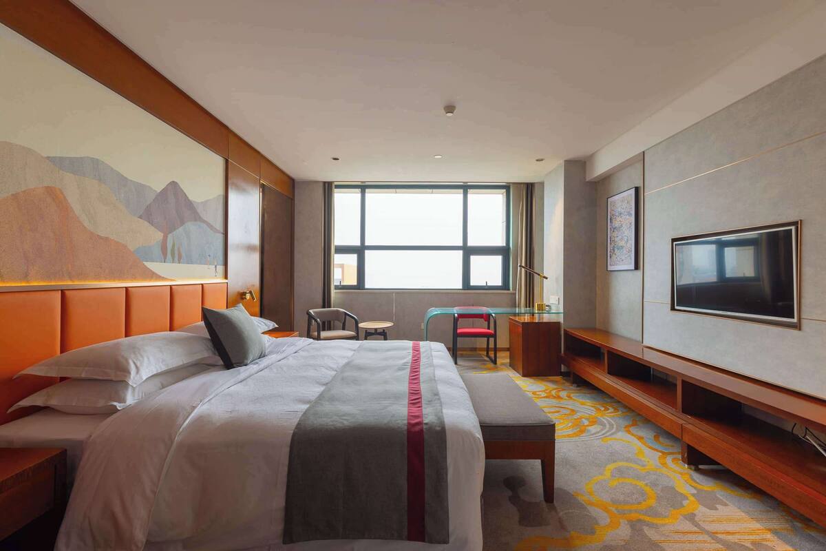 A hotel room with a large bed, a TV, a desk, and a window with a view.