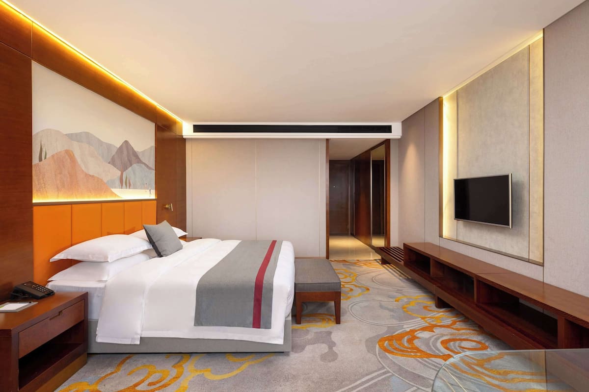 A modern hotel room with a large bed, a TV mounted on the wall, and a desk with a telephone.