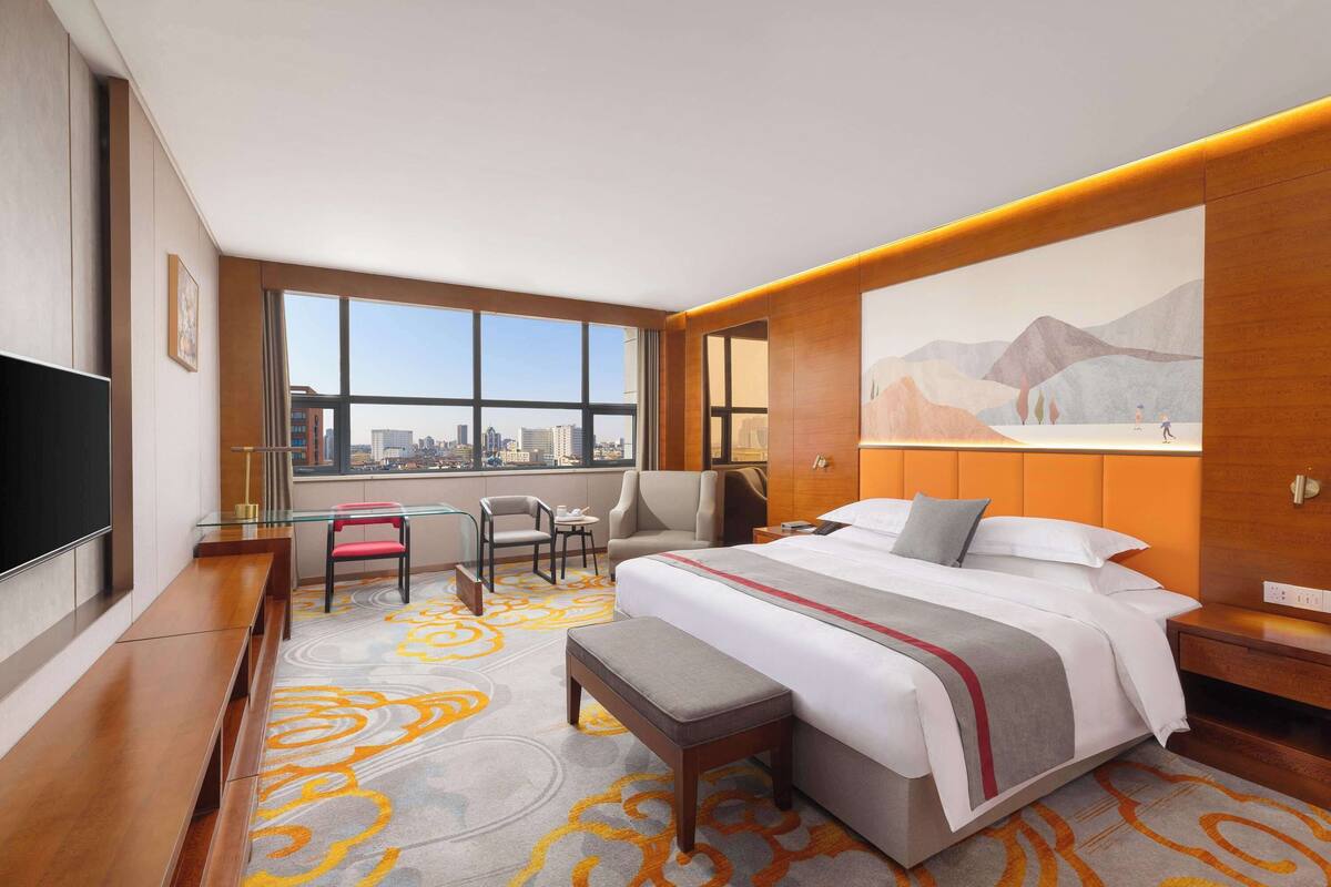 A hotel room with a large bed, a desk with two chairs, a TV, and a city view.